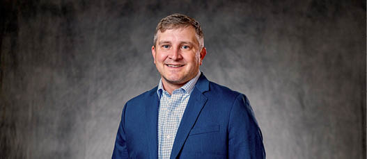 A man wearing a blue suit and a white shirt is smiling for the camera. AI generated content