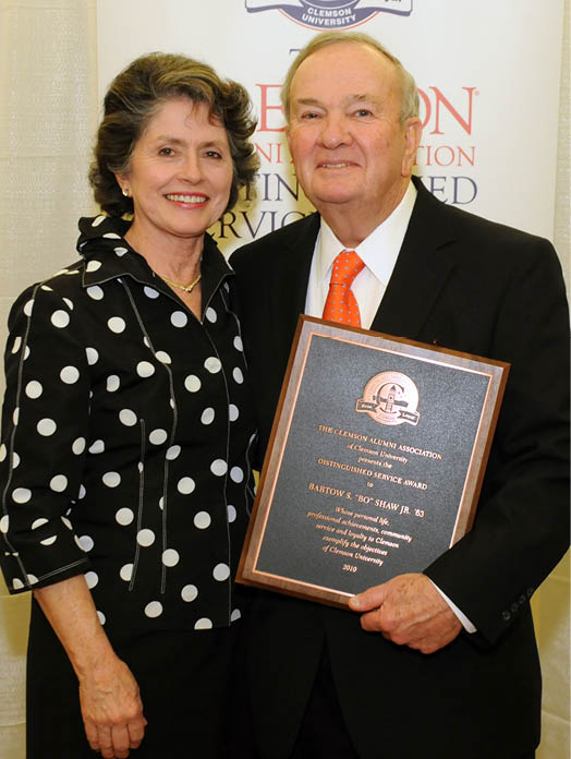 A man and woman are standing next to each other, holding a plaque. The man is wearing a suit and tie. AI generated content